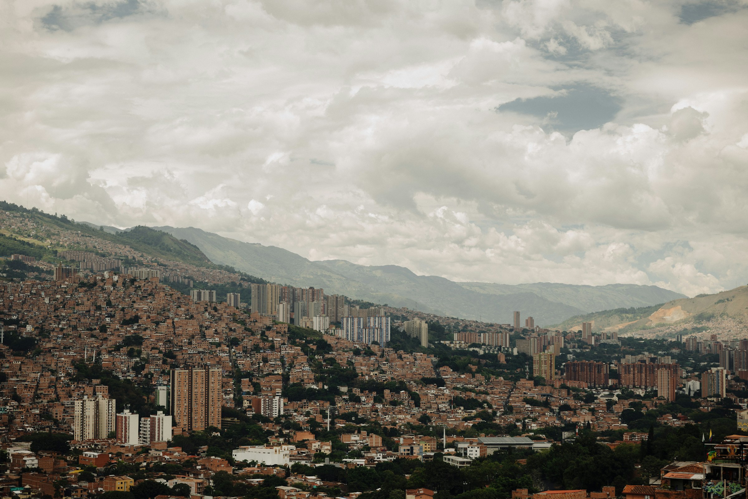 Barrios y edificios de Medellín rodeados de montañas bajo un cielo con nubes.